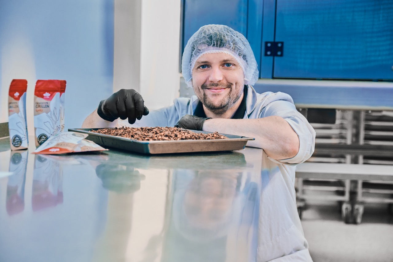 Foto des Unternehmensgründers in Arbeitskleidung. Vor ihm befindet sich ein Tablett gefüllt mit Grillen, sowie drei Packungen geröstete Grillen.